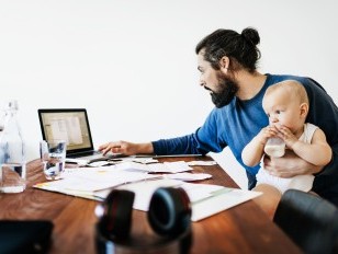 Mann im Home Office mit Kleinkind im Arm
